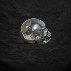 Echter Pyrit-Totenkopf in Seitenansicht auf dunklem Steinuntergrund – glänzender Wikinger-Schädel aus massivem Pyrit, Symbol für Stärke, Mut, Schutz und Erdverbundenheit.