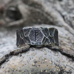 Runen Ring aus Edelstahl mit eingravierter Rune – liegend auf Felsen im natürlichen Wikinger-Stil – strukturierte, dunkle Oberfläche mit gehämmertem Muster – Symbol für Stärke und Schutz, hochwertiger Wikinger Runenschmuck von NORDSKULLS.