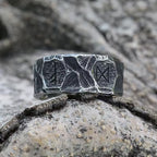 Runen Ring aus Edelstahl mit mehreren eingravierten Runen – liegend auf Felsen im Wikinger-Stil – strukturierte, dunkle Oberfläche mit antiker Optik – symbolträchtiger Ring für Stärke und Schutz, hochwertiger Wikinger Runenschmuck von NORDSKULLS.