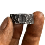Wikinger Runen Ring aus Edelstahl mit eingravierter Rune – gehalten von einer kräftigen, leicht schmutzigen Männerhand im nordischen Stil – strukturierte, gehämmerte Oberfläche, echtes Runenschmuck-Design von NORDSKULLS.