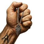Muskulöse Wikinger-Hand mit Runen-Tattoo hält eine Vegvisir Arrowhead Wikinger Halskette aus Metall, graviert mit dem nordischen Schutzsymbol.