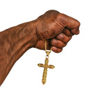 Wikinger Halskette RAGNARS CROSS aus Edelstahl – goldfarbenes Kreuz mit filigranem Muster, gehalten in einer starken Männerhand